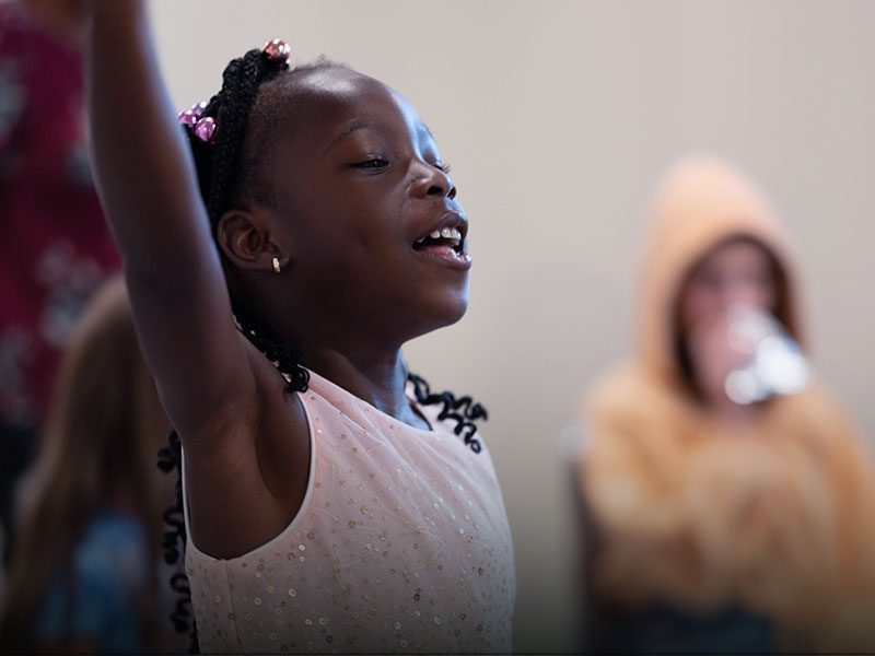 A young girl singing and lifting her hands