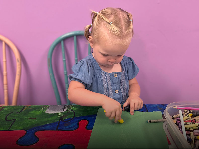 A young girl colouring with crayons